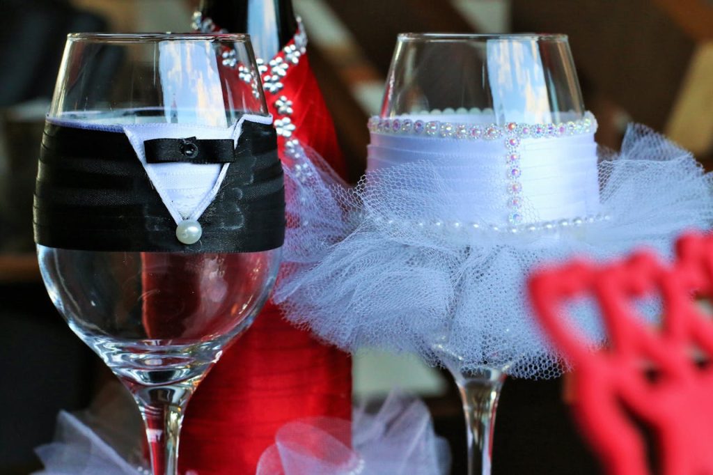 two-clear-bridge-and-groom-wine-glasses-1253142 Close-up of fancy wine glasses dressed in tuxedo and gown decor, perfect for weddings.